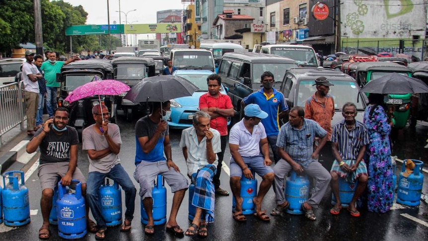 People sit on empty gas cylinders as they block a road to protest against thel shortage of fuel in Sri Lanka