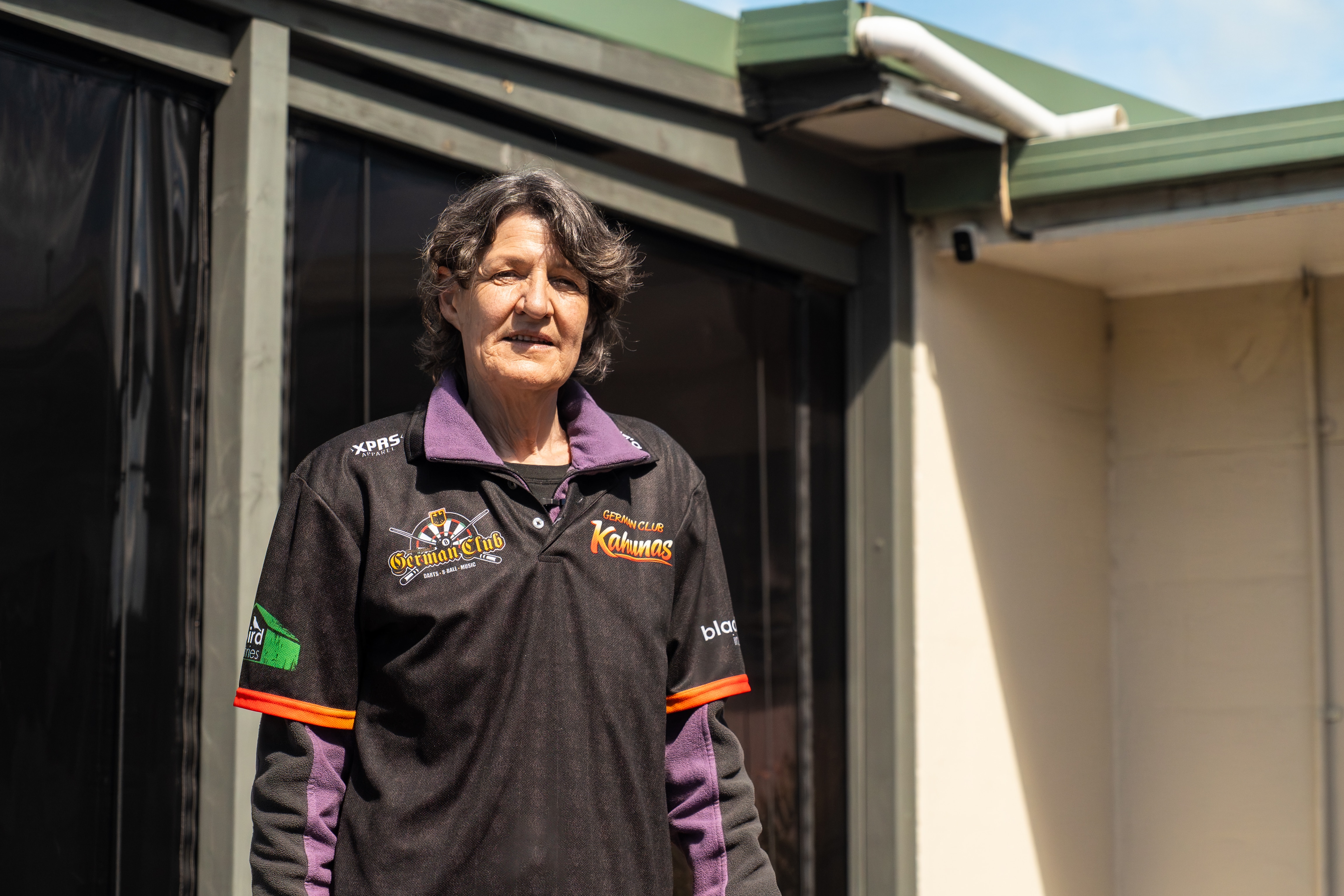 A woman stands in front of a residential property, a security camera can be seen behind her.