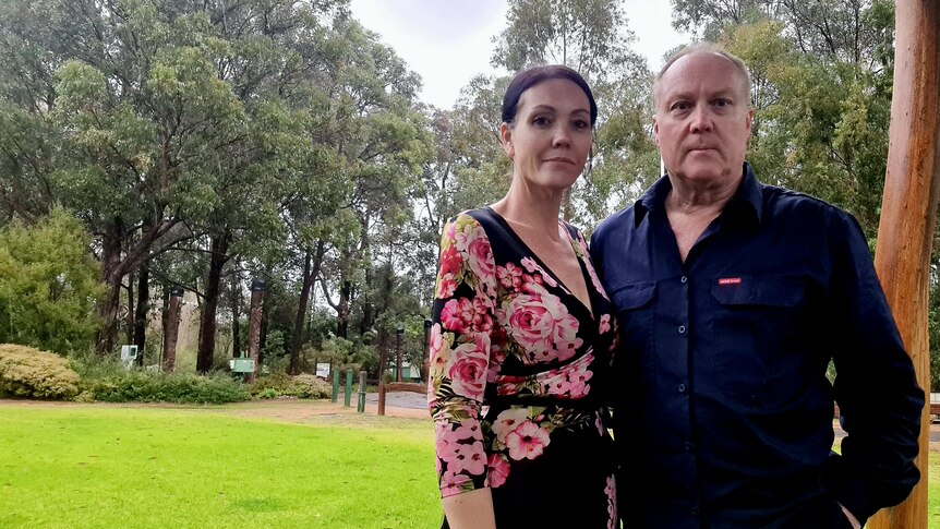 Dark-haired woman standing next to man in front of natural bushland.