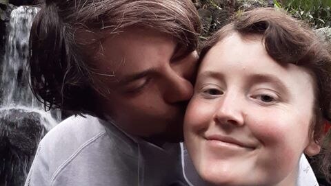 Lachlan Humphris kisses his girlfriend on the cheek in front of waterfall