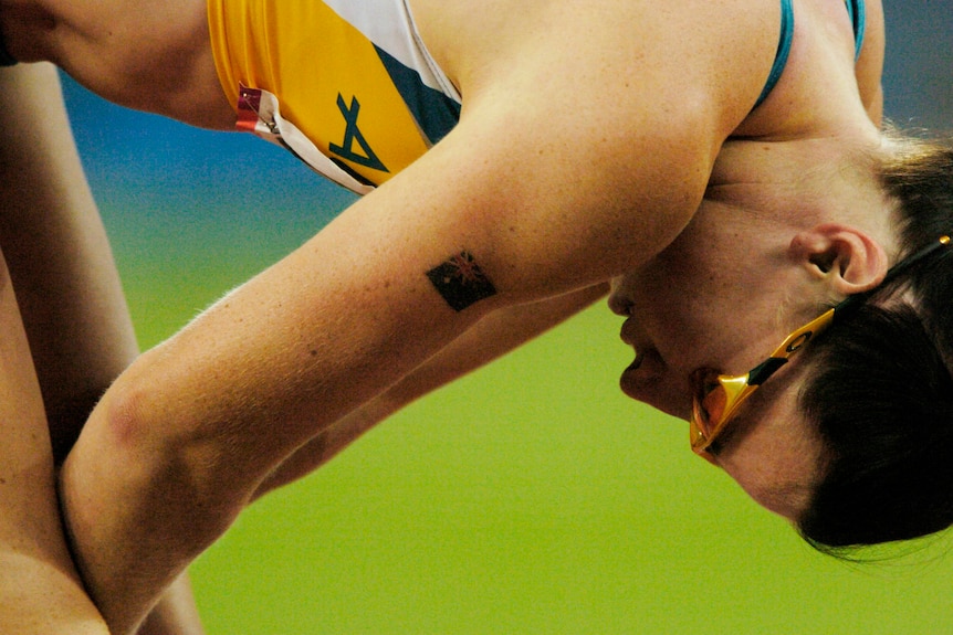 An athlete in yellow and green Australia colours leans over in dispair