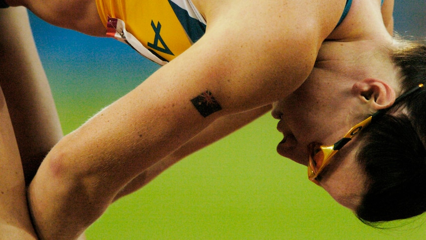 An athlete in yellow and green Australia colours leans over in dispair