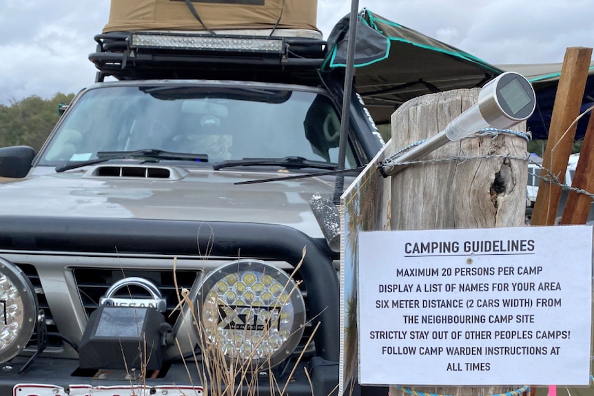 A four-wheel drive beside a large white sign with rules about camping at a festival.
