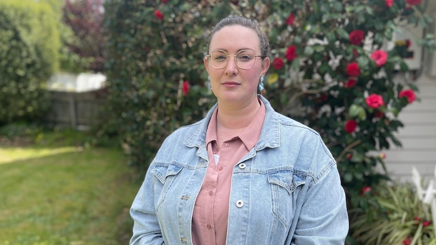 A woman in glasses standing in front of a rose bush