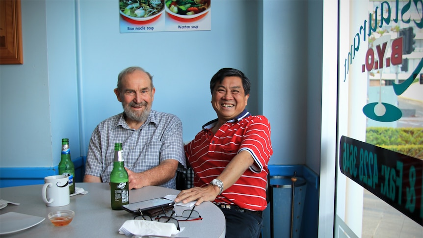 Ben Morris and Trinh Hung Phat sit in Trinh's restaurant, smiling with beers on the table.