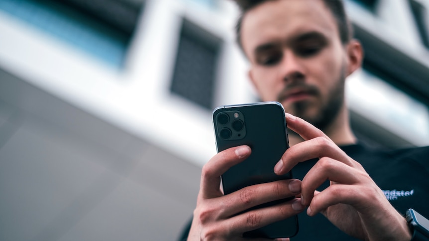 A young man wearing a jumper looks at an iPhone.