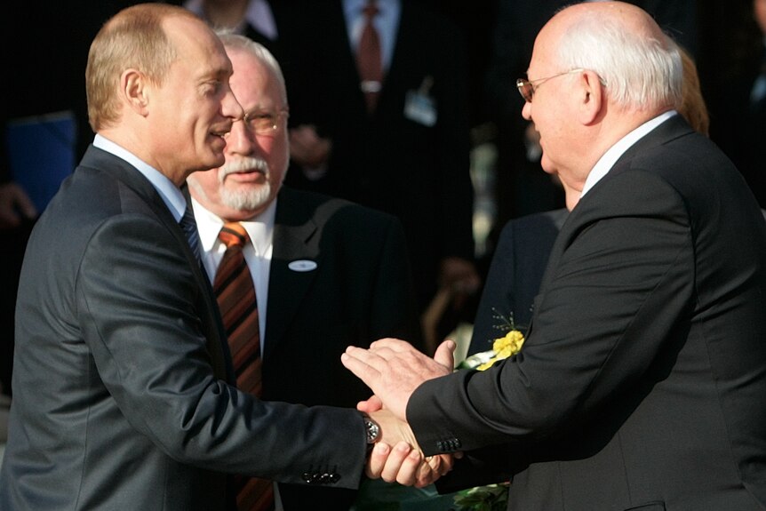 Vladimir Putin (L) wearing a suit shakes the hand of Mikhail Gorbachev in a suit. 