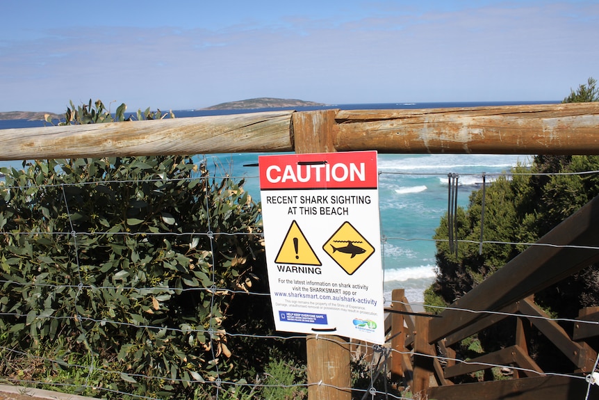 A signed fixed to a fence, overlooking the ocean