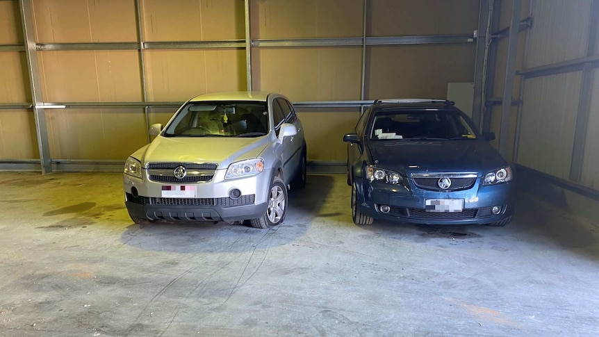 A silver four-wheel-drive and a blue sedan are pictured inside a garage. Each has minor damage.