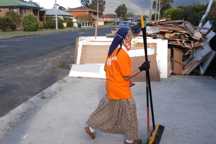 A woman in an orange T-shirt with a broom
