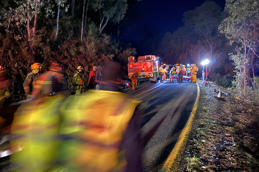 Emergency crews mill about a road in the side of a hill