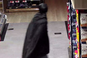 A man wearing a black cape and a mask in a supermarket aisle