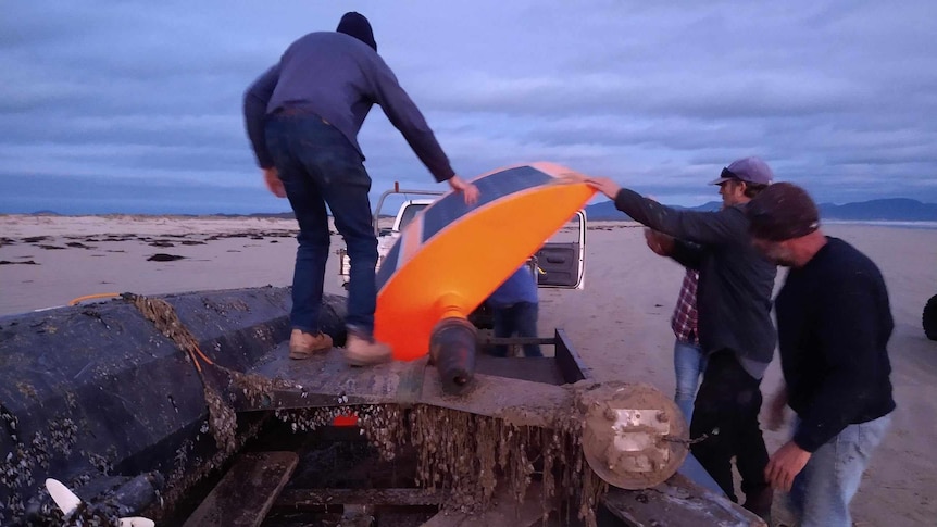 Four people load a sail drone on to the back of a utility.