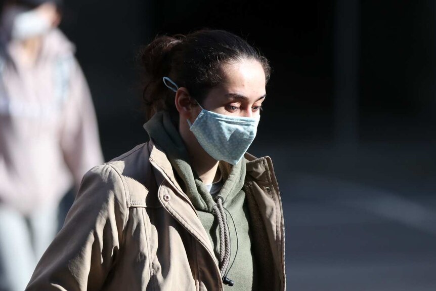 A woman with her hair tied back and wearing a mask walks in Melbourne.