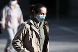 A woman with her hair tied back and wearing a mask walks in Melbourne.
