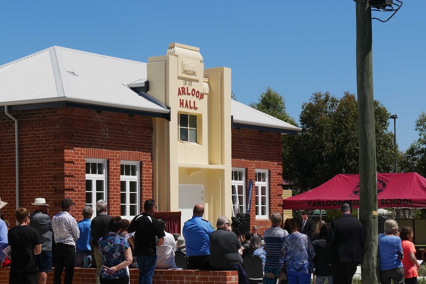 A crowd of people gather outside a municipal building on a bright, sunny day.