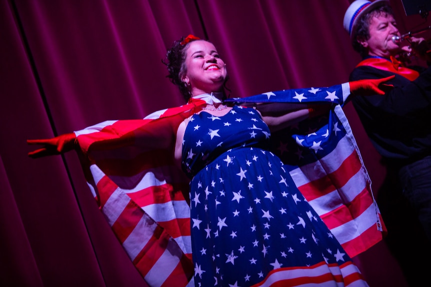 Singer draped in American flag looks to the back rows, arms wide