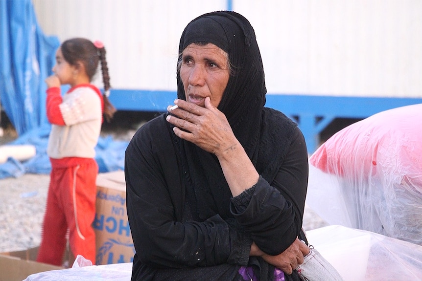 A woman dressed in black, smoking a cigarette in the Debaga camp, North Iraq.
