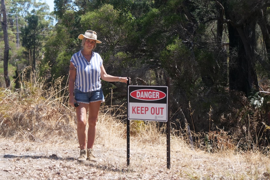A woman stands beside a sign that says danger keep out.