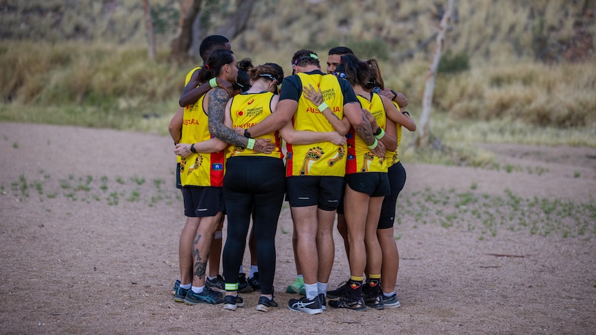 A group of runners huddle together with arms around each other