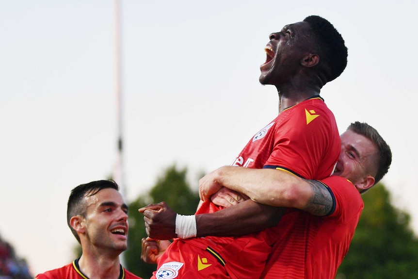 Al Hassan Toure, wearing a red shirt, screams whilst being picked up and carried by a teammate