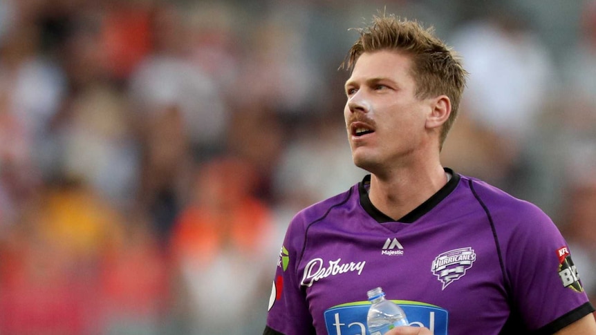 James Faulkner holds a clear bottle of water at his side and looks up wearing a purple kit