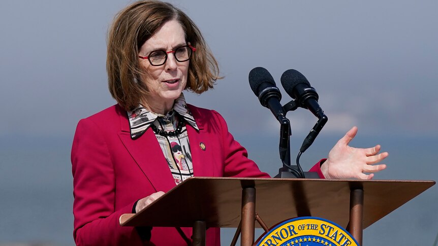 A woman in a red jacket speaking at a lectern