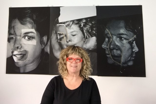 A woman, wearing red glasses, stands in front of a photomontage