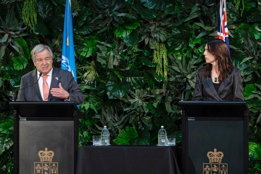 Antonio Guterres stands on a podium next to Jacinda Ardern.