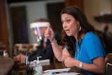 A woman gestures while she sits at a desk and speaks