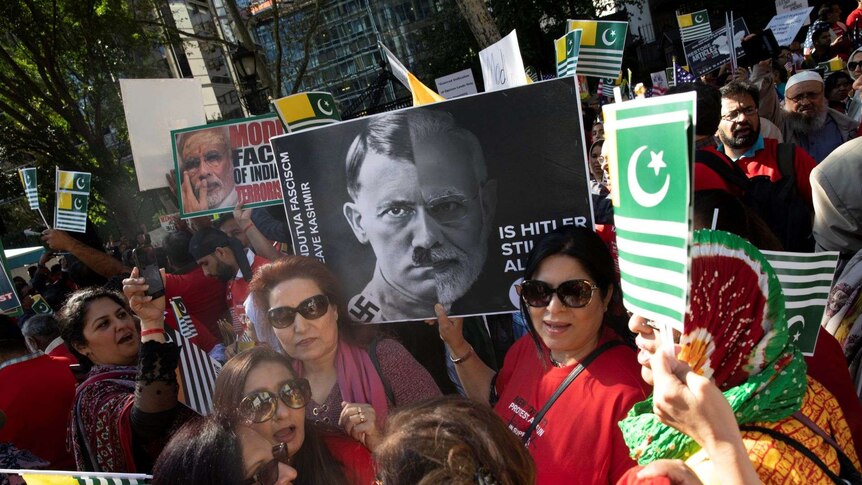 A crowd hold flags of Azad Kashmir. A woman holds a poster depicting both Adolf Hitler and Indian Prime Minister Narendra Modi.