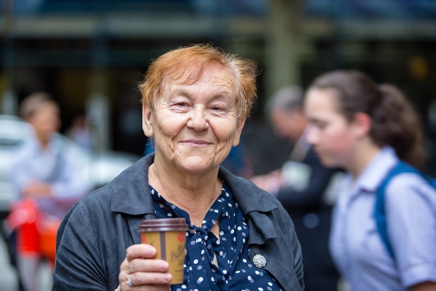A lady smiles as she holds up a coffee outside Pellegrini's.