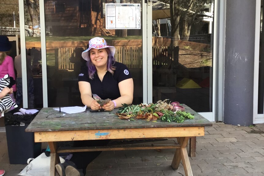 A woman in a lavender bucket hat sits at an outdoor picnic table in a courtyard.