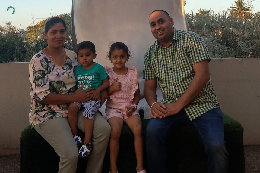 A woman and man smile as they pose for a photo with their young son and daughter, who is giving a thumbs up.