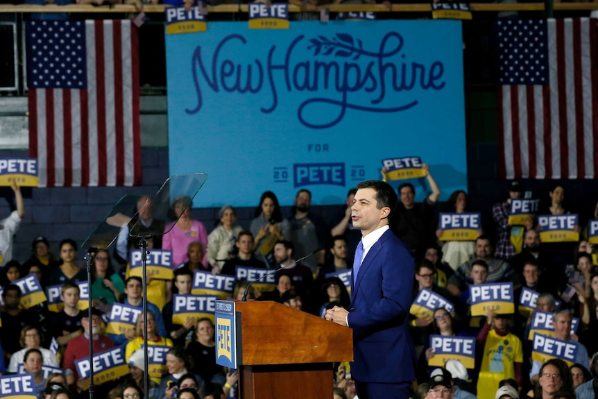 Pete Buttigieg standing at a podium with a "New Hampshire for Pete" sign behind him