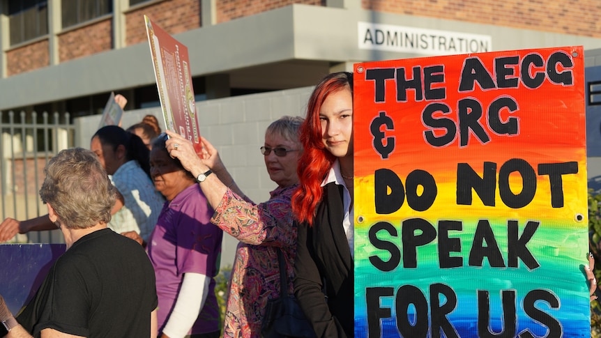 A teenage girl looks at the camera while holding a protest sign next to a group of protesters