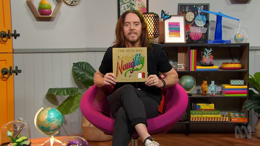 Tim Minchin holds up story book, Sometimes You Have To Be a Little Naughty