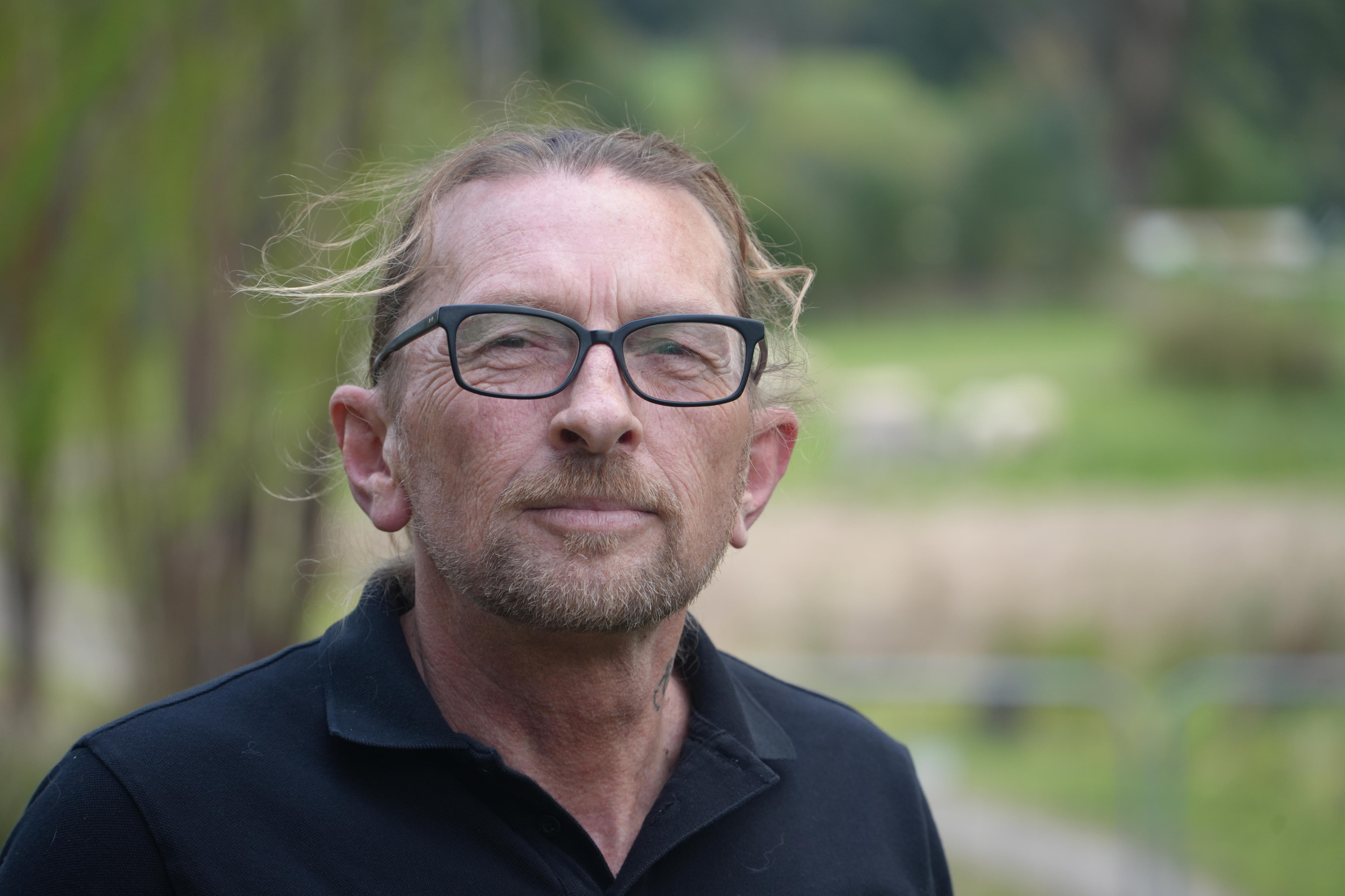 A man with long wiry hair and glassess looks at the camera