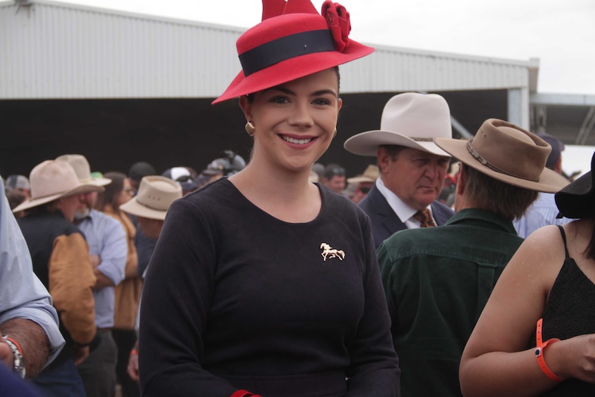 A woman wearing a red fascinator and a horse brooch smiles for the camera.