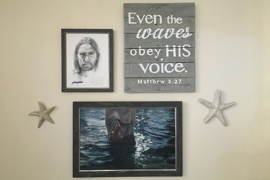 A portrait of Jesus is among the religious artworks hanging on a wall. Another reads: Even the waves obey His voice