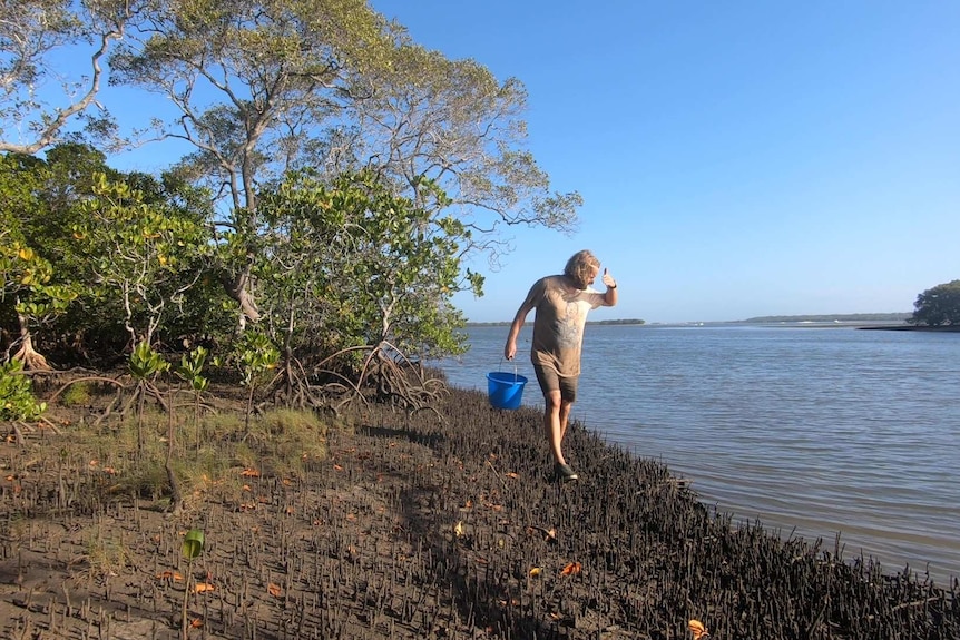 A man covered in mud looking into a creek.