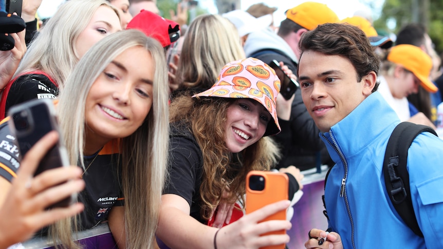 Two female fans take selfies with a male Formula One driver
