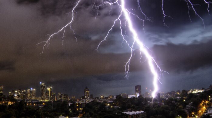 A large bolt of lightning snakes through a dark sky towards the Sydney cityscape.