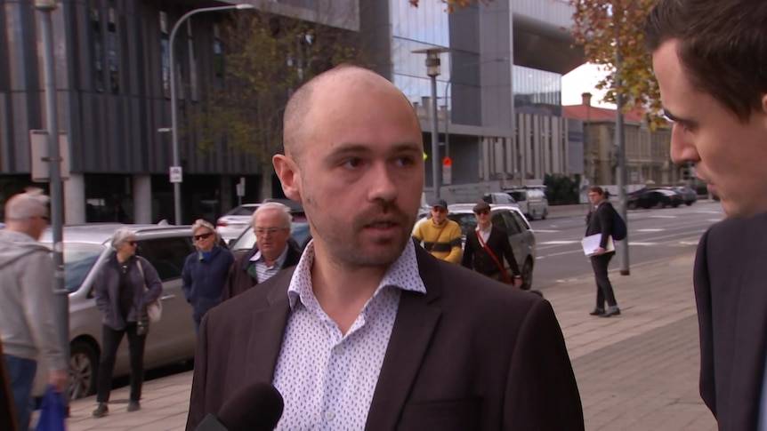 A bald man wearing a black suit jacket and white shirt