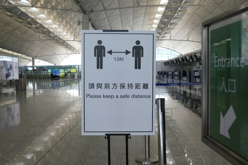 A sign in an empty airport terminal reminds people to "please keep a safe distance" apart
