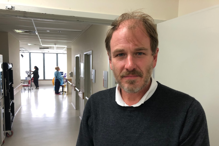 A man stands in a hospital corridor.