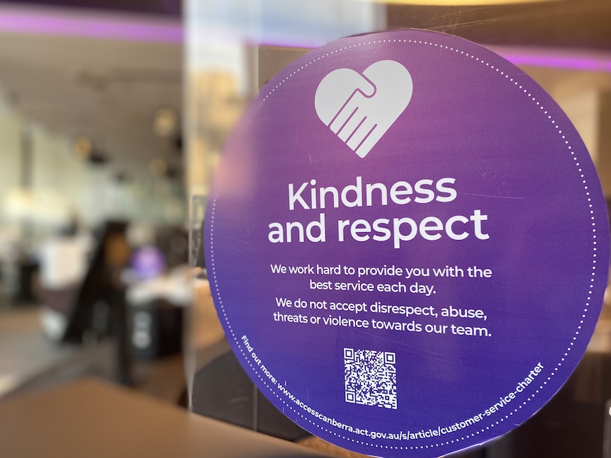A sign says "kindness and respect" and is stuck in a window of an office.