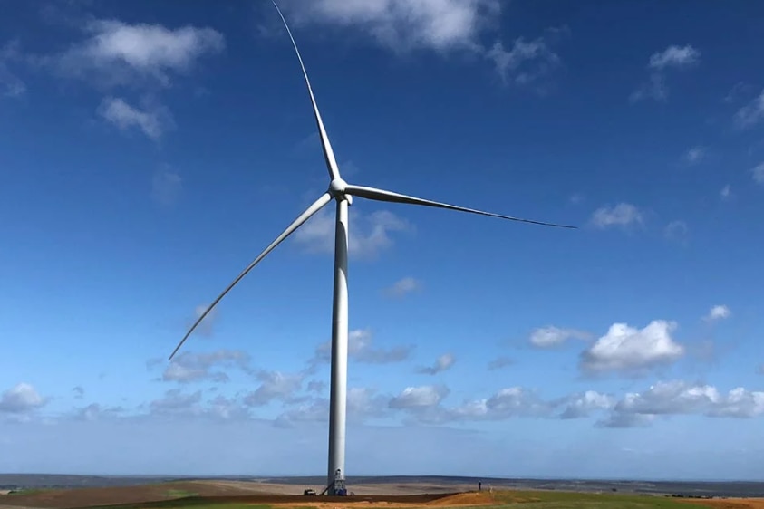 Shot from the ground looking up at a three-bladed wind turbine against the backdrop of a blue sky.