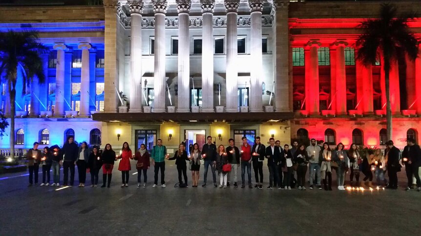 A line of people in front of a building lit up in blue, white and red.