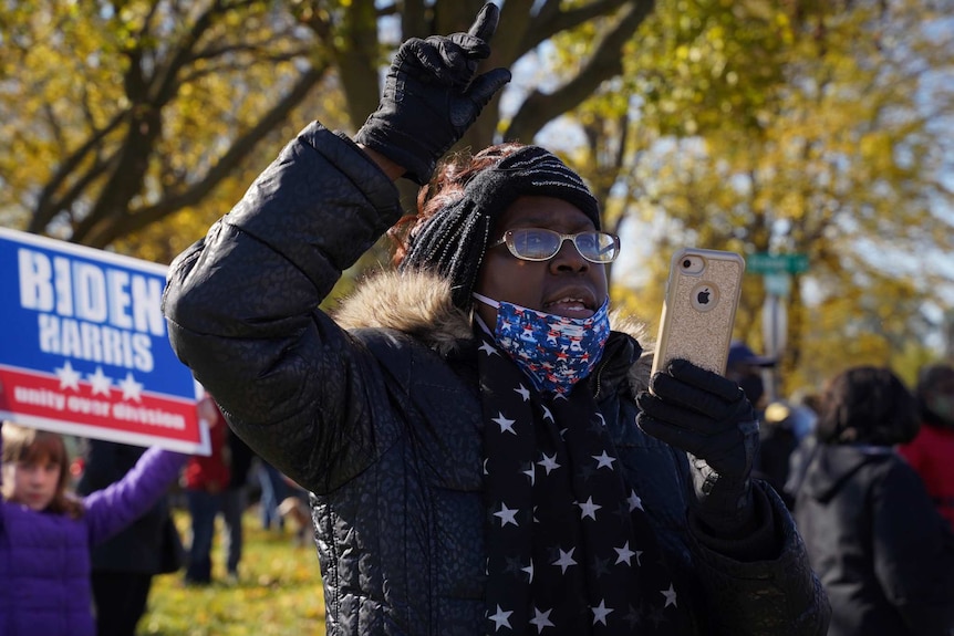 A Joe Biden supporter shouts, with a finger in the sky, and a phone in her hand outside a rally in Flint, Michigan.